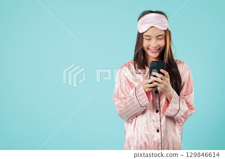 Young asian woman, happy using phone in pajama, relaxing ready for sleep, smiling while resting at home looking at her mobile, after a good sleep at night, headshots isolated studio blue background Young asian woman, happy using phone in pajama, relaxing ready for sleep, smiling while resting at home looking at her mobile, after a good sleep at night, headshots isolated studio blue background 129846614