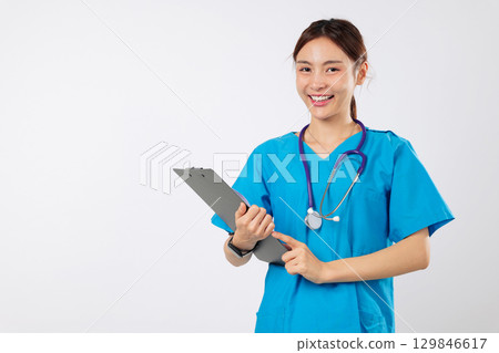 Smiling young doctor healthcare medical uniform asian woman holds clipboard stethoscope and the friendly nurse is excited to promote healthcare and the caring work of nurse, isolated white background Smiling young doctor healthcare medical uniform asian woman holds clipboard stethoscope and the friendly nurse is excited to promote healthcare and the caring work of nurse, isolated white background 129846617