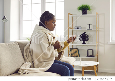 Sick African American woman with fever looks at thermometer that shows very high temperature 129846726