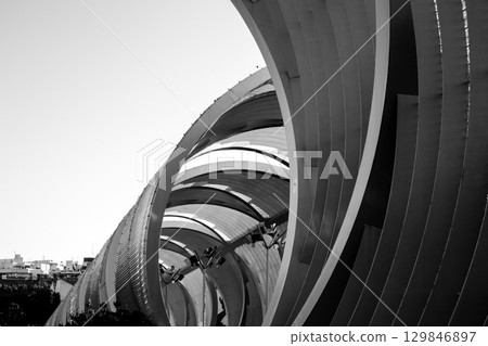 A monochrome image capturing architectural curves and lines in a modern structure. Black and white architectural detail of a modern building, showing curved lines and abstract shapes under sunlight. A monochrome image capturing architectural curves and lines in a modern structure. Black and white architectural detail of a modern building, showing curved lines and abstract shapes under sunlight. 129846897