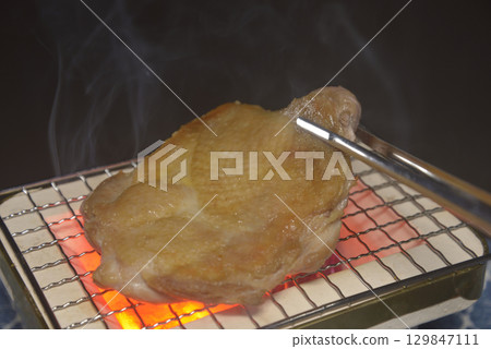 Grilling chicken thighs on a smoky charcoal grill 129847111