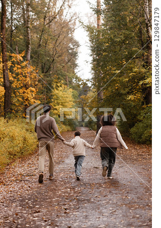 Back view of happy family of three walking in beautiful autumn park. Back view of happy family of three walking in beautiful autumn park. 129847179