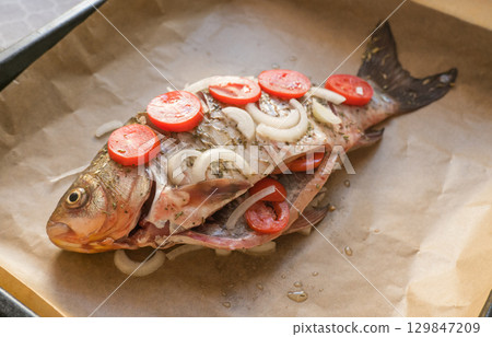 Fresh whole river crucian fish on parchment with tomatoes and spices ready for baking. 129847209