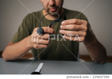 Cropped shot of male hands holding smartwatch inductive charger, preparing to power up smart watch, sitting at table on isolated background. Concept of healthy lifestyle. Cropped shot of male hands holding smartwatch inductive charger, preparing to power up smart watch, sitting at table on isolated background. Concept of healthy lifestyle. 129847300