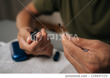 Close-up of young man cleaning electronic cigarette with cotton swab, focusing on proper maintenance and hygiene for vaping device sitting at home table. Concept of vaping device remain 129847319