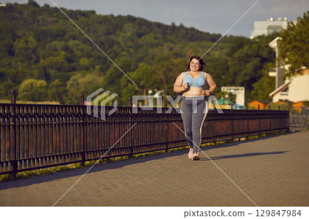 Happy overweight woman running on bridge during her outdoor fitness workout in city Happy overweight woman running on bridge during her outdoor fitness workout in city 129847984
