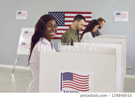 Happy american voter woman putting her ballot in bin on election day standing at vote center. 129848010