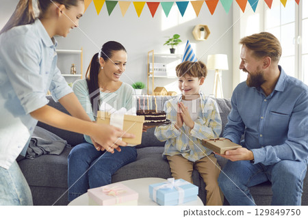 Happy family sitting on sofa at home and congratulating their smiling child boy on birthday party Happy family sitting on sofa at home and congratulating their smiling child boy on birthday party 129849750