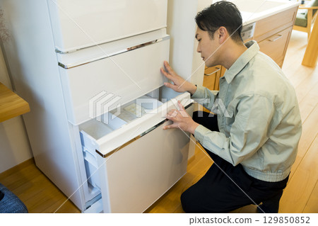 A man in work clothes installing a refrigerator A man in work clothes installing a refrigerator 129850852