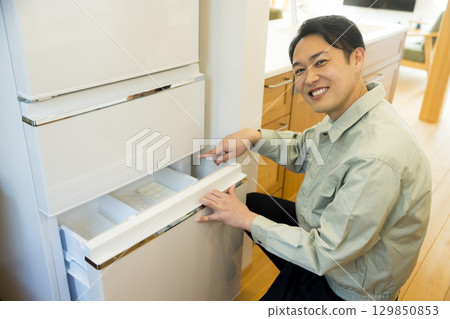 A man in work clothes installing a refrigerator 129850853