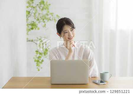 一位年輕女子在客廳一邊使用筆記型電腦一邊思考 一位年輕女子在客廳一邊使用筆記型電腦一邊思考 129851221