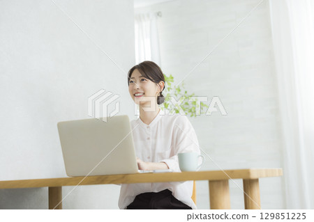 一位年輕女子在客廳一邊使用筆記型電腦一邊思考 129851225