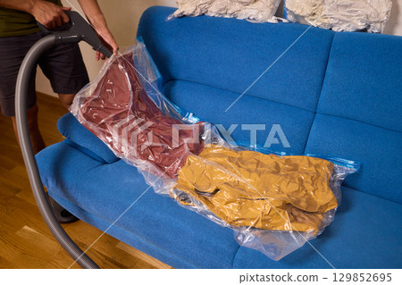 A man on a cozy blue couch uses a vacuum sealer to pack his clothes, enjoying a relaxing day 129852695