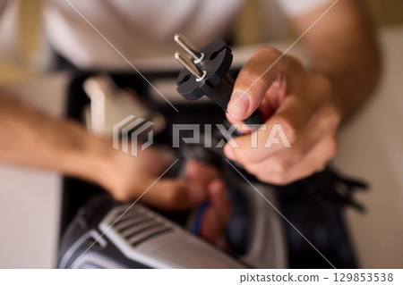 A Person is Holding an Electrical Plug with Various Tools in the Background Present A Person is Holding an Electrical Plug with Various Tools in the Background Present 129853538