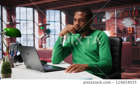 Teleworker fixing his back posture and suffering a muscle cramp at home desk, feeling fatigued and uncomfortable with backache. Freelancer experiences office syndrome, discomfort. Camera B. Teleworker fixing his back posture and suffering a muscle cramp at home desk, feeling fatigued and uncomfortable with backache. Freelancer experiences office syndrome, discomfort. Camera B. 129854035