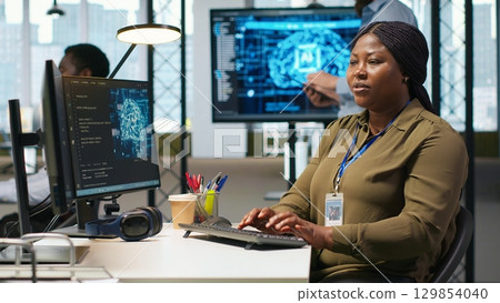 Female software developer using artificial intelligence to optimize performance and forecast issues. Woman in office training machine learning models using computer, camera A 129854040