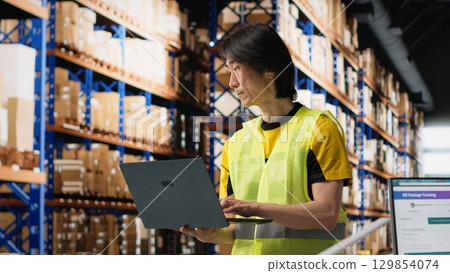 Multiethnic staff processing e-commerce orders and reviewing invoices, organizing cargo goods inside industrial warehouse space with storage racks. Smooth delivery and quality control. Camera B. Multiethnic staff processing e-commerce orders and reviewing invoices, organizing cargo goods inside industrial warehouse space with storage racks. Smooth delivery and quality control. Camera B. 129854074