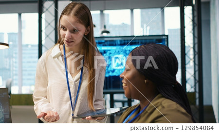 Manager teaching young technician how to develop software and optimize code using AI. Team leader guiding intern in office on how to use artificial intelligence to resolve bottlenecks, camera A 129854084