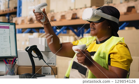 African american woman working with VR tech system to process orders and manage parcel shipment tracking, hands free inventory control. Virtual reality guarantees fast delivery. Camera B. African american woman working with VR tech system to process orders and manage parcel shipment tracking, hands free inventory control. Virtual reality guarantees fast delivery. Camera B. 129854126