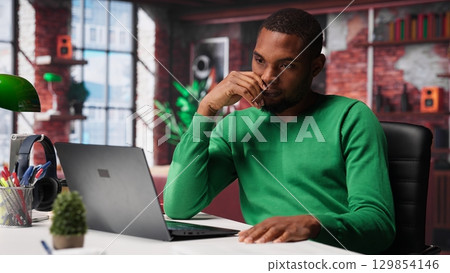 Teleworker fixing his back posture and suffering a muscle cramp at home desk, feeling fatigued and uncomfortable with backache. Freelancer experiences office syndrome, discomfort. Camera A. 129854146