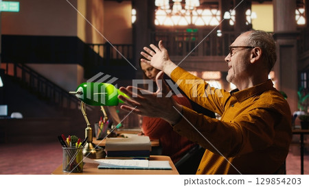 Experienced man rehearsing a theatre script in a quiet library, studying lines with commitment and emotion and practicing character development for role preparation. Acting skills. 129854203