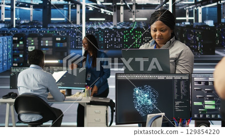 Annoyed data center admin having trouble doing node tree programming. Irked woman in server room having glitching issues while using predictive AI visualization systems on notebook, camera A 129854220