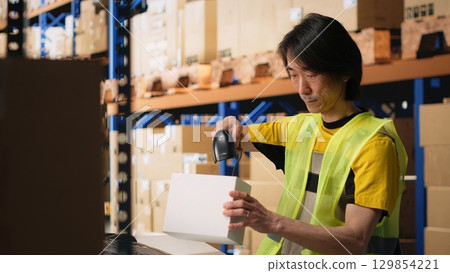 Asian employee scanning shipping labels and barcodes on packages, manages labeling registration with a scanner and handling inventory tracking. E-commerce fulfillment center. Camera B. Asian employee scanning shipping labels and barcodes on packages, manages labeling registration with a scanner and handling inventory tracking. E-commerce fulfillment center. Camera B. 129854221