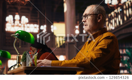 Elderly man with a respiratory problem having a panic attack in the library, struggling to learn due to a discomfort or breathing issue. Senior person in distress, hyperventilation. Elderly man with a respiratory problem having a panic attack in the library, struggling to learn due to a discomfort or breathing issue. Senior person in distress, hyperventilation. 129854326