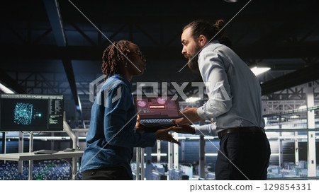 Stressed technicians in server room fighting each other after detecting hacking attempt targeting critical systems. Engineering team members under pressure by virus activity arguing, Stressed technicians in server room fighting each other after detecting hacking attempt targeting critical systems. Engineering team members under pressure by virus activity arguing, 129854331