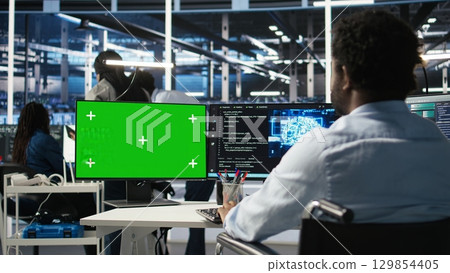 Data center admin in wheelchair using AI node tree software on green screen PC to minimize system downtime. Server hub employee in disability using visual programming tool on mockup computer, camera A Data center admin in wheelchair using AI node tree software on green screen PC to minimize system downtime. Server hub employee in disability using visual programming tool on mockup computer, camera A 129854405