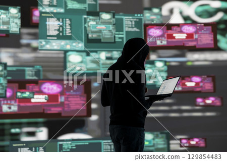 Young guy hacker breaking into a system in stealth mode by programming code, bypassing firewalls and exploiting vulnerabilities in network security to carry out cyber attack and infiltration. Young guy hacker breaking into a system in stealth mode by programming code, bypassing firewalls and exploiting vulnerabilities in network security to carry out cyber attack and infiltration. 129854483