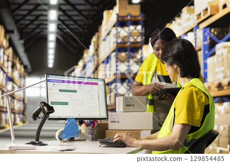 African american supervisor asking asian man about the delivery status, discussing about tracking info on a distribution software. E commerce warehouse relies on smart logistics systems. 129854485
