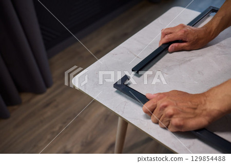 Hand Assembling a Frame on a Beautiful and Modern Table in a Creative Workspace Hand Assembling a Frame on a Beautiful and Modern Table in a Creative Workspace 129854488