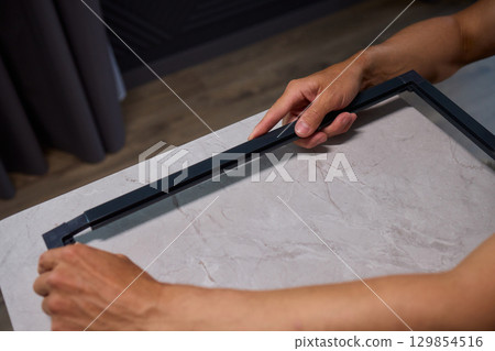Hand Assembling a Frame on a Beautiful and Modern Table in a Creative Workspace 129854516