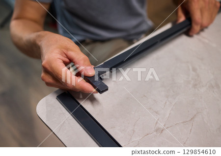 Hand Assembling a Frame on a Beautiful and Modern Table in a Creative Workspace Hand Assembling a Frame on a Beautiful and Modern Table in a Creative Workspace 129854610
