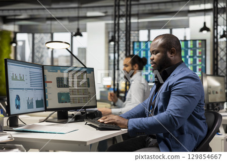 African american businessman analyzing performance metrics and graphs, preparing business reports to optimize management strategy and guarantee corporate growth, innovation and achievement. 129854667