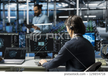 Admin in data center speaks in headset mic, troubleshooting rigs connectivity issues using AI. IT expert doing tech support in server hub, talking in remote call, auditing systems for vulnerabilities Admin in data center speaks in headset mic, troubleshooting rigs connectivity issues using AI. IT expert doing tech support in server hub, talking in remote call, auditing systems for vulnerabilities 129854716