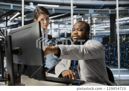 Data center manager supervising engineer running diagnostic scripts on computer, examining gear. Server room supervisor overseeing worker using PC to evaluate rackmounts performance metrics 129854728