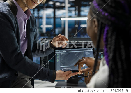 Close up of programmers coding on tablet in data center, updating AI driven automation scripts. IT workers using device in server room, programming artificial intelligence algorithms, debugging gear 129854749