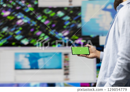 Young guy looks at green screen on phone as a user interface, checking online presence on social platforms. Male Influencer working on creativity and online engagement in a digital world. Young guy looks at green screen on phone as a user interface, checking online presence on social platforms. Male Influencer working on creativity and online engagement in a digital world. 129854779