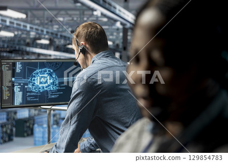 Data center expert assisting users with artificial intelligence enhanced troubleshooting, delivering technical support. Man in server farm chatting in headset mic with users in need of assistance 129854783