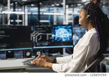 Data center admin speaking in headset mic, using AI assistant to provide user technical support. Server hub IT professional assisting clients during remote call using artificial intelligence Data center admin speaking in headset mic, using AI assistant to provide user technical support. Server hub IT professional assisting clients during remote call using artificial intelligence 129854784
