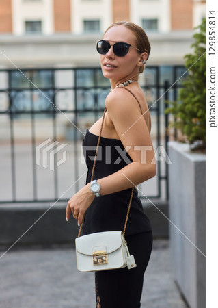 A Stylish and Fashionable Woman Dressed in Elegant Black Attire, Complete with Chic Sunglasses A Stylish and Fashionable Woman Dressed in Elegant Black Attire, Complete with Chic Sunglasses 129854814