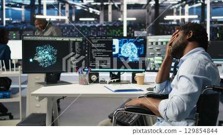 Man in wheelchair dissatisfied with server farm AI analytics metrics. Data center admin with paraplegia frustrated by glitches while automating tasks using node tree programming tool, camera A 129854844