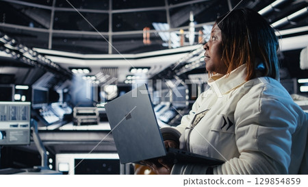Astronaut returning from planet surface taking helmet off, talking with colleague using laptop to verify parameters. Cosmonaut finishing expedition chatting with coworker updating flight log Astronaut returning from planet surface taking helmet off, talking with colleague using laptop to verify parameters. Cosmonaut finishing expedition chatting with coworker updating flight log 129854859