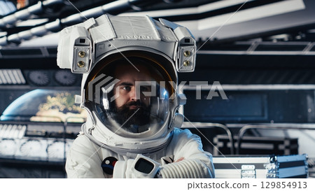Portrait of astronaut wearing helmet before stepping out for scheduled operations outside space station. Man in cosmonaut suit in starship approaching distant planetary surface Portrait of astronaut wearing helmet before stepping out for scheduled operations outside space station. Man in cosmonaut suit in starship approaching distant planetary surface 129854913