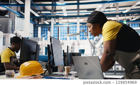Photovoltaics factory technician designing CAD models and technical sketches for solar modules on laptop. Woman engineer ensures solar panel designs for efficiency and manufacturability. Camera B. 129854969
