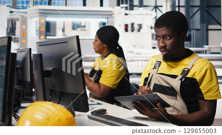 PC based solar technician reviews automation data in production factory, manufacturing industry focused on renewable energy. Worker tracks solar panels and machine performance. Camera B. 129855003