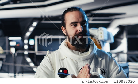Cheerful astronaut doing videocall with Earth command center while aboard orbit station, sharing mission update. Happy cosmonaut talks with ground center team during communication link Cheerful astronaut doing videocall with Earth command center while aboard orbit station, sharing mission update. Happy cosmonaut talks with ground center team during communication link 129855020