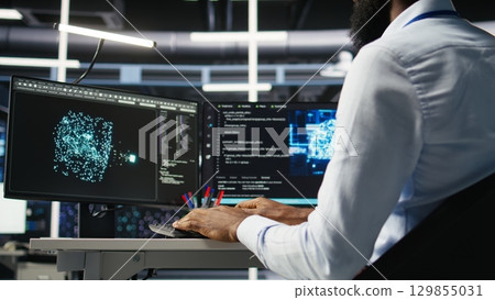 Data center computer scientist at desk using AI deep learning algorithms to analyze datasets. Server room IT specialist typing on PC keyboard, using artificial intelligence neural networks, camera A 129855031